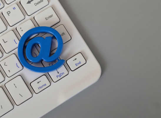 Simbolo della chiocciola e-mail blu posizionato sopra i tasti direzionali di una tastiera bianc